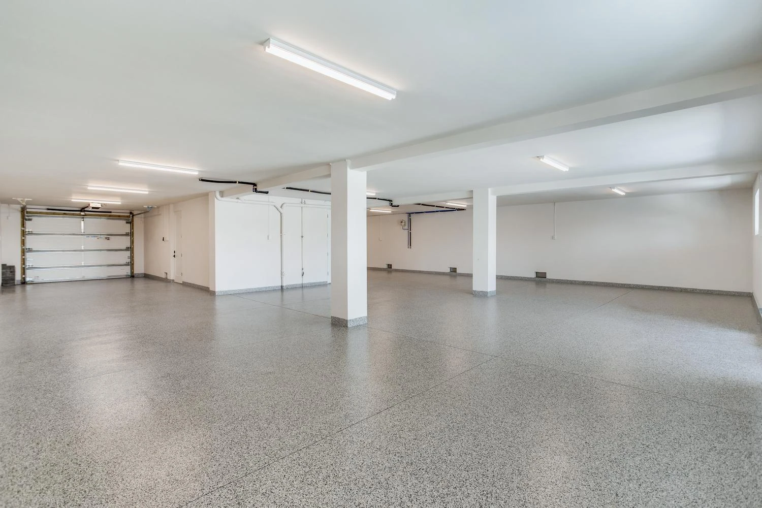 Enclosed ground level of an elevated coastal home with an epoxy floor, structural columns and a garage door